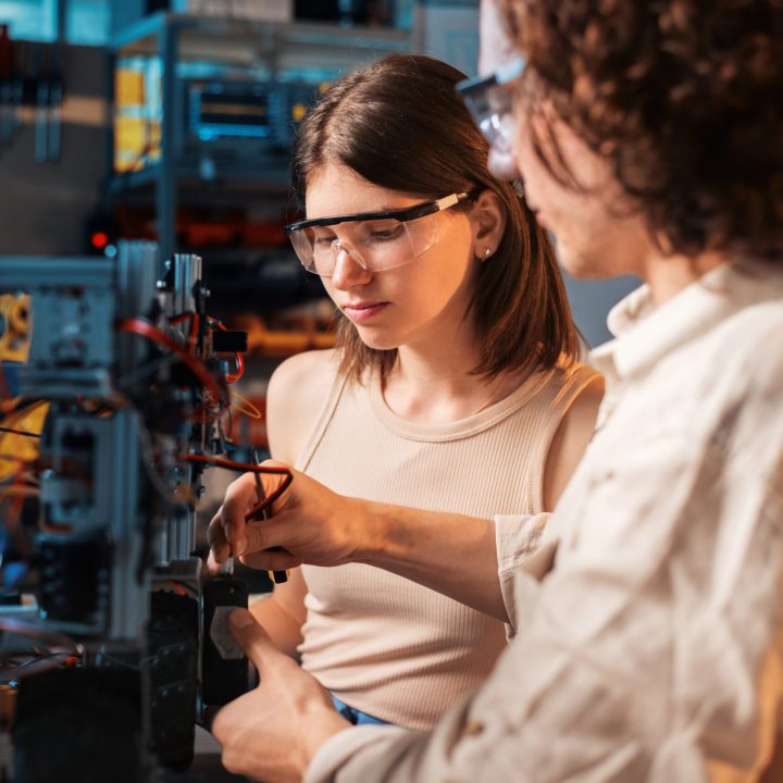 Young man and woman in protective glasses doing experiments in robotics in a laboratory. Robot on the table